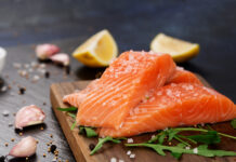 La place du poisson dans une alimentation saine et équilibrée Raw fillet of salmon with sea salt, lemon and pepper on black stone background