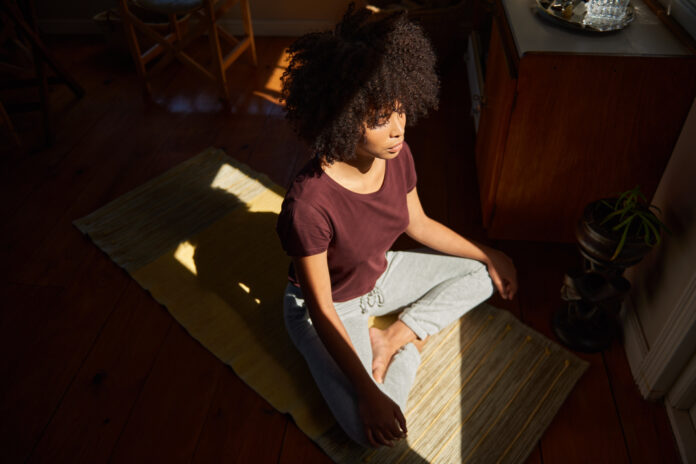 Young African woman meditating by a sunny window at home