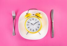 Maîtriser la chrononutrition pour affiner votre silhouette abdominale Retro alarm clock on plate with fork and knife isolated on pink
