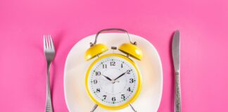 Maîtriser la chrononutrition pour affiner votre silhouette abdominale Retro alarm clock on plate with fork and knife isolated on pink