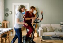 Comment bien choisir votre vélo d’appartement pour séniors ? Mature female physical therapist assisting elderly woman on exercise bike at nursing home