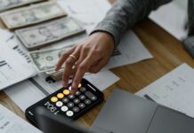 Rachat assurance vie : comment réduire vos impôts ? Main d'un épargnant effectuant une simulation de fiscalité sur son smartphone devant une liasse de billets et des documents financiers.