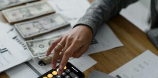 Rachat assurance vie : comment réduire vos impôts ? Main d'un épargnant effectuant une simulation de fiscalité sur son smartphone devant une liasse de billets et des documents financiers.