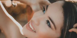 Alimentation et éclat : les secrets d’un teint parfait Portrait lumineux d'une jeune femme souriante et radieuse, regardant vers le haut, avec un visage éclatant et des yeux bleus dans une chaude lumière du soleil.